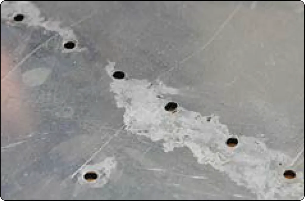 Aircraft metal surface showing corrosion damage, with visible discoloration and deterioration caused by chemical or environmental reactions