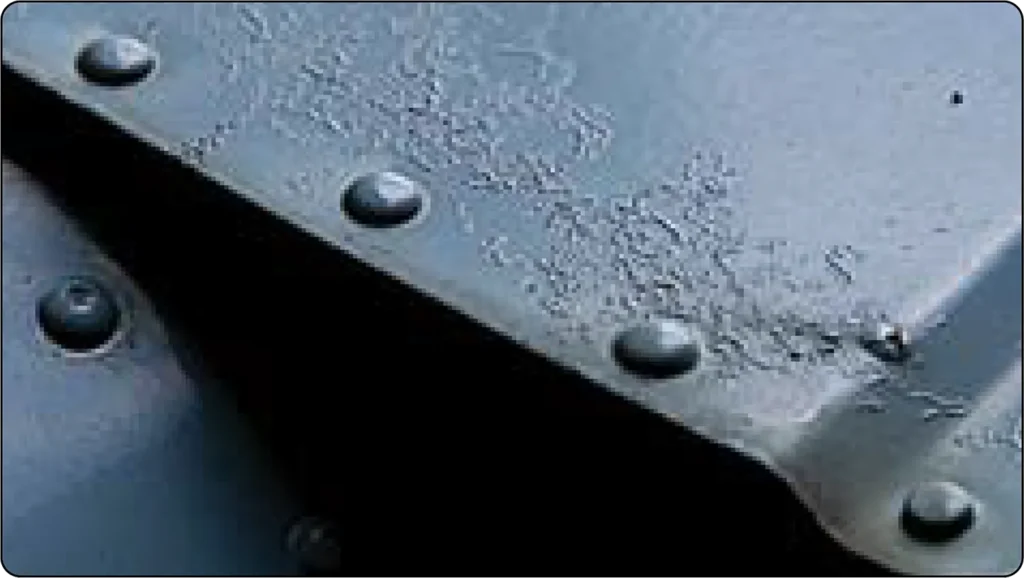 Close-up of filiform corrosion on a coated metal surface, showing thread-like corrosion tracks spreading beneath the protective finish