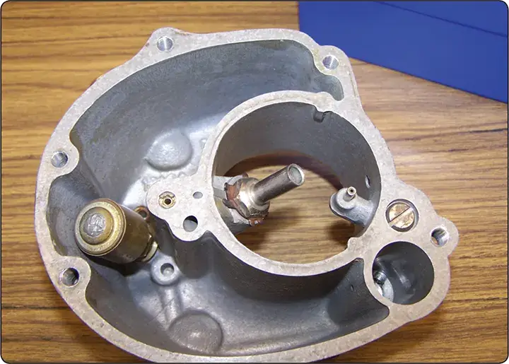 Float chamber of a carburetor shown with the float removed, revealing the internal bowl