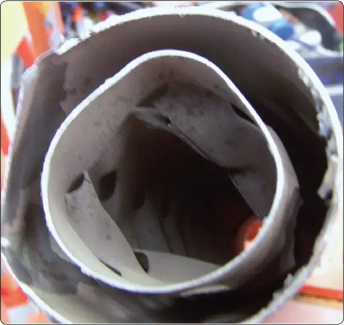 Illustration showing internal muffler failure caused by erosion and carbon buildup, with broken material obstructing exhaust flow